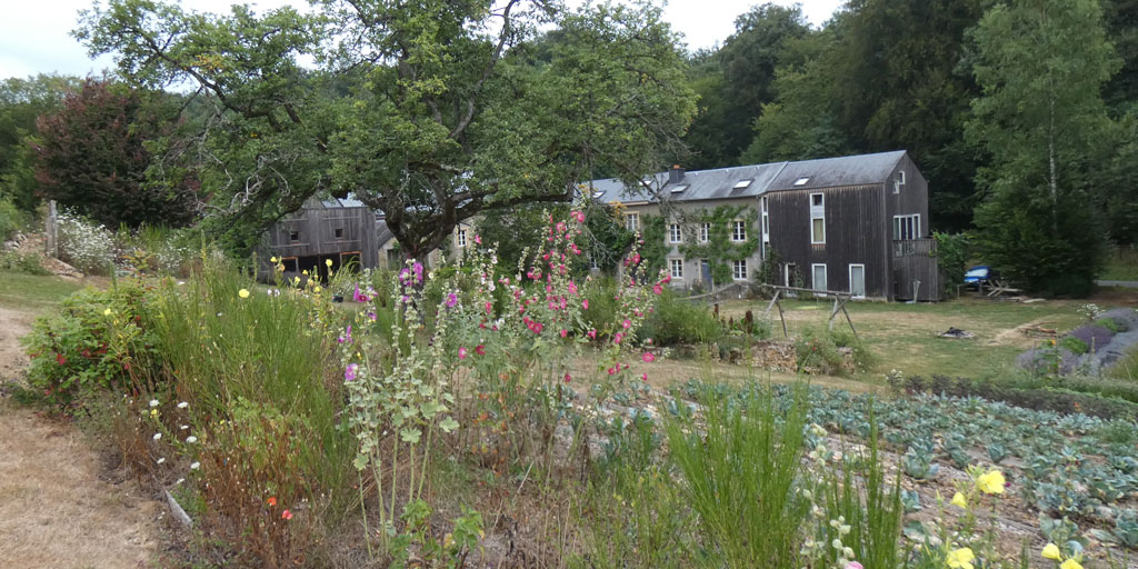 Vue sur les bâtiments de la ferme. On peut y voir l'installation de panneaux photovoltaïques et un aperçu des jardins alentours.